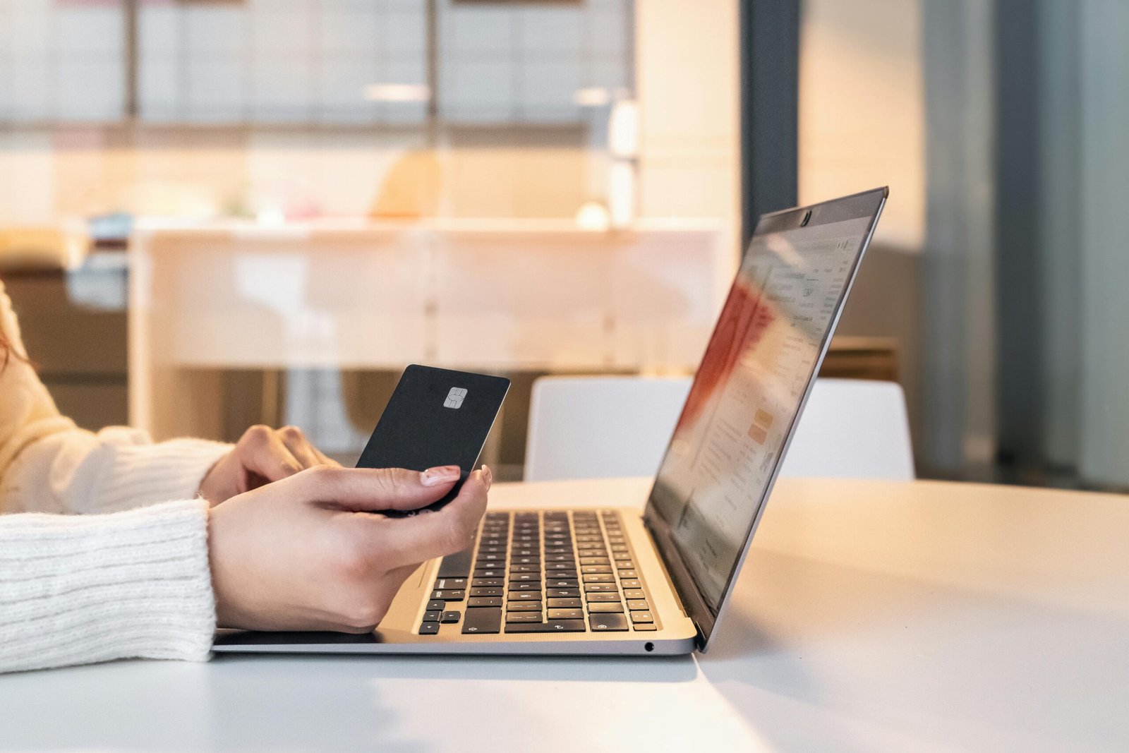 Home A woman using a credit card and laptop for online shopping in a modern indoor setting.